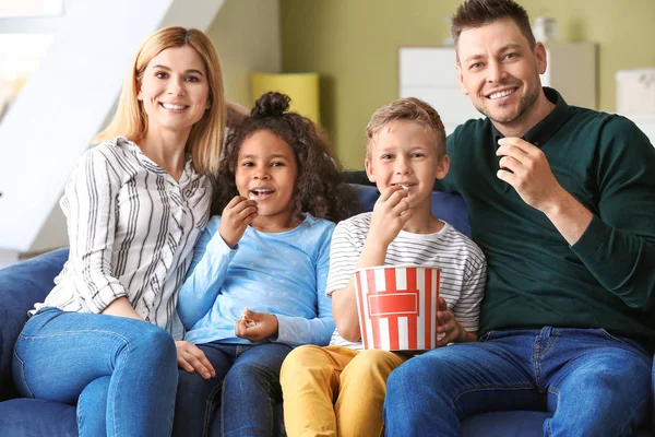 Happy couple with little adopted children watching TV at home — Stock Photo, Image