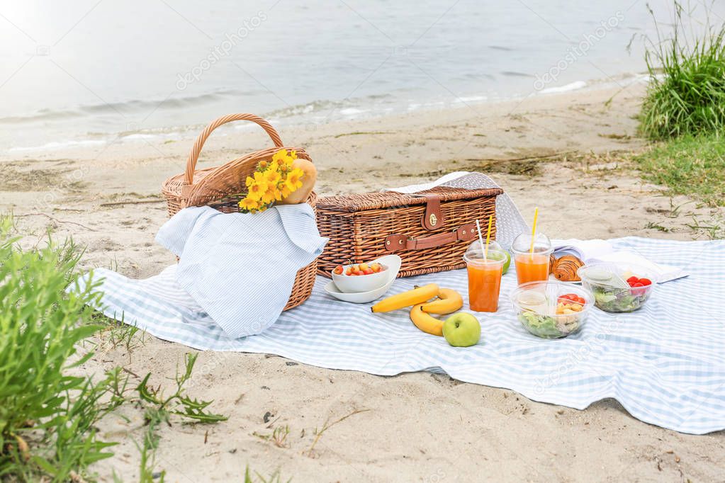 Wicker baskets with tasty food and drink for romantic picnic near river