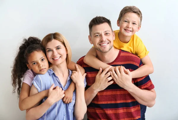 Pareja feliz con niños adoptados sobre fondo claro — Foto de Stock