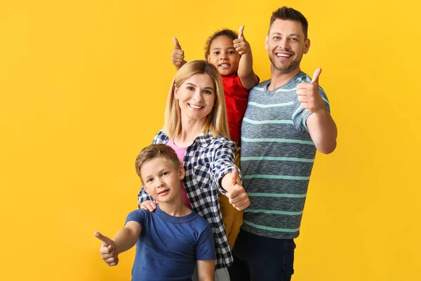 Casal feliz com crianças adotadas pouco mostrando polegar para cima no fundo de cor — Fotografia de Stock