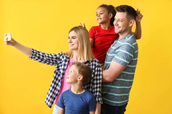 Boldog pár kis örökbefogadott gyermekek figyelembe selfie a színes háttér — Stock Fotó