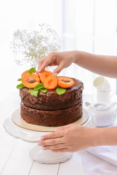 Vrouw versieren smakelijke chocoladetaart met abrikozen — Stockfoto