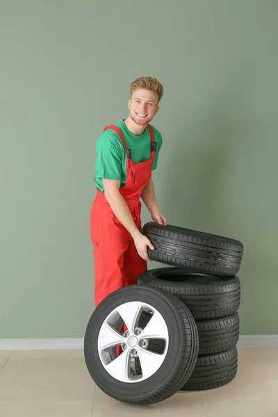 Jovem mecânico masculino com pneus de carro perto da parede de cor — Fotografia de Stock