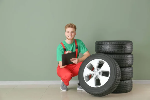 カラーウォールの近くに車のタイヤを持つ若い男性の整備士 — ストック写真