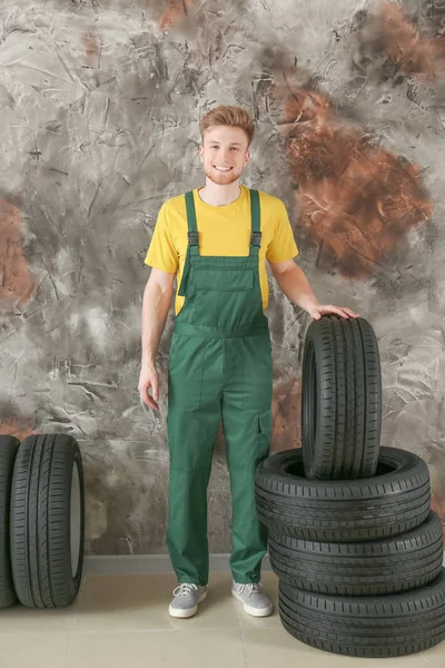 Ung manlig mekaniker med bildäck nära grunge Wall — Stockfoto