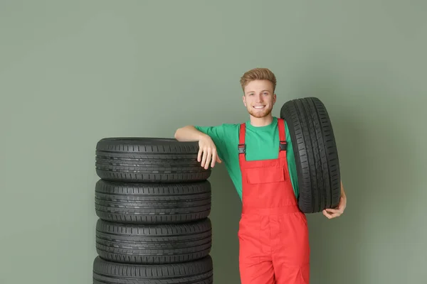 色の背景に車のタイヤを持つ若い男性の整備士 — ストック写真