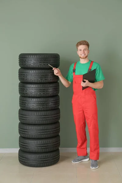 Молодий чоловік-механік з шинами автомобіля біля кольорової стіни — стокове фото