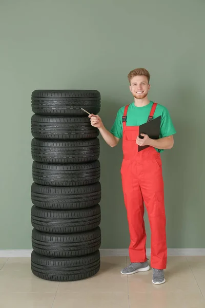 Junger männlicher Mechaniker mit Autoreifen in der Nähe von Farbwand — Stockfoto