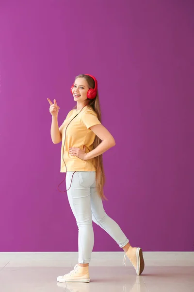 Beautiful young woman listening to music against color wall — Stock Photo, Image