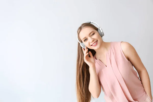 Mooie jonge vrouw luisteren naar muziek op lichte achtergrond — Stockfoto