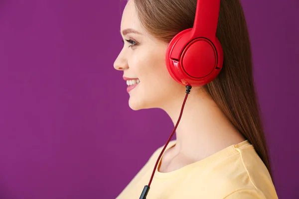 Mooie jonge vrouw luisteren naar muziek tegen kleur achtergrond — Stockfoto