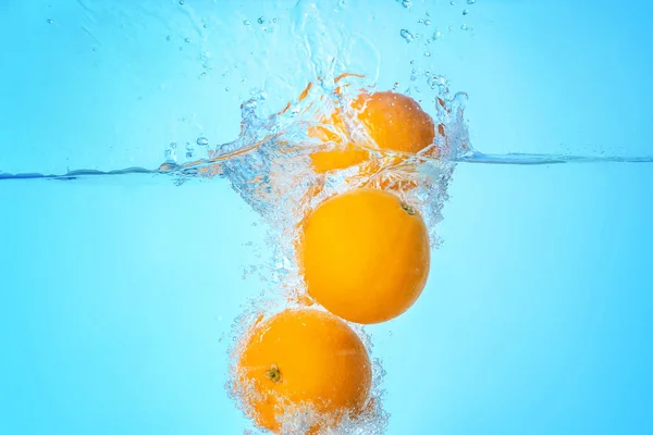 Het vallen van sinaasappelen in water op lichte achtergrond — Stockfoto