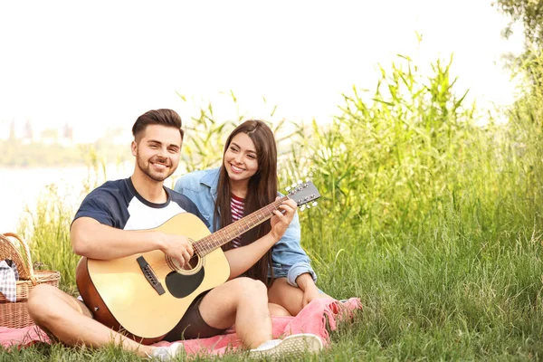 Pareja joven con guitarra en el picnic en el parque — Foto de Stock