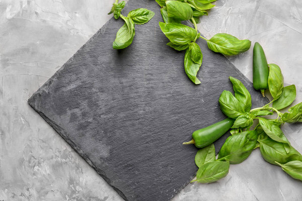 Slate plate with fresh basil and peppers on grey background