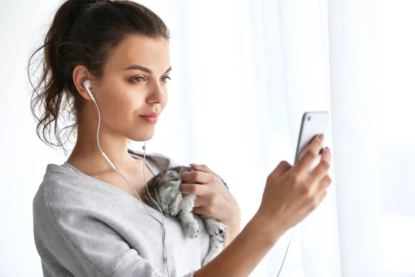 Beautiful young woman with cute little kitten listening to music at home — Stock Photo, Image