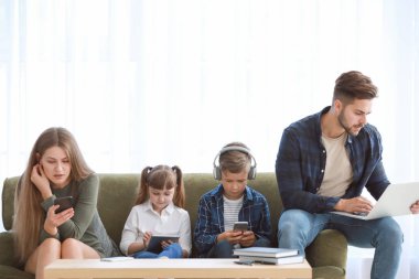 Evde kanepede oturan cihazlar ile modern teknolojilere bağımlı aile