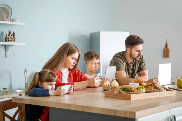 Сім'я з залежністю від сучасних технологій, що сидять за столом на кухні — стокове фото