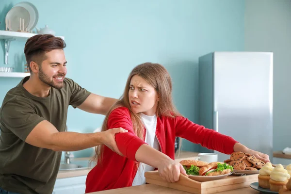 Giovane uomo che cerca di prendere vassoio con il cibo da donna dipendente in cucina — Foto Stock