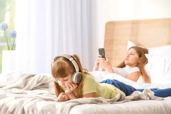 Little girl with addiction to modern technologies lying with mobile phone on bed at home — Stock Photo, Image