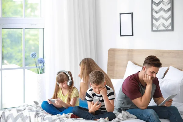 Familia adicta a las tecnologías modernas con dispositivos sentados en la cama en casa —  Fotos de Stock