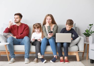 Evde kanepede oturan cihazlar ile modern teknolojilere bağımlı aile