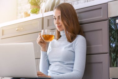 Mutfakta çay içen dizüstü ile güzel genç kadın