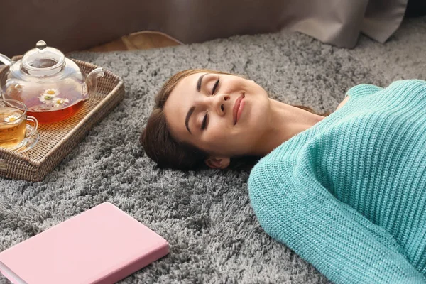 Mulher bonita com chá e livro deitado no tapete em casa — Fotografia de Stock