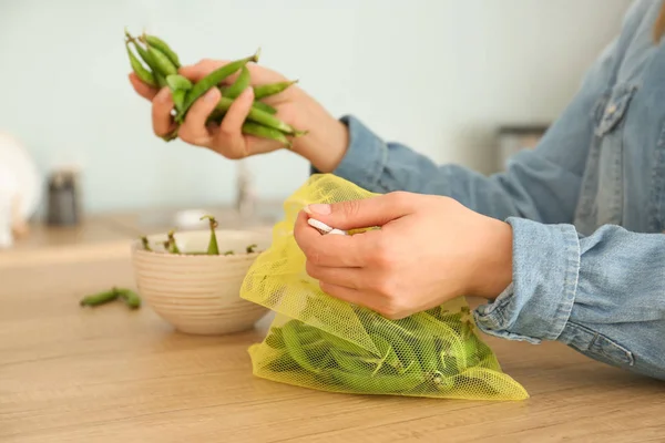 キッチンでエコバッグに新鮮なエンドウ豆のポッドを入れる女性 — ストック写真