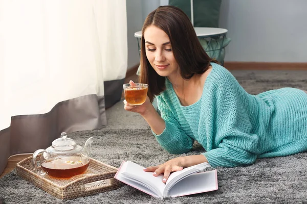 Hermosa mujer joven bebiendo té mientras lee libro en casa — Foto de Stock