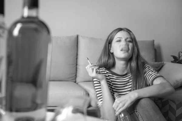 Молодая женщина с зависимостью от алкоголя и сигарет расслабляется дома — стоковое фото