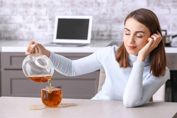 Sleepy young woman spilling tea on kitchen table — Stock Photo, Image