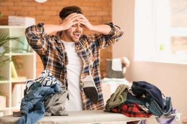 Stresli genç adam evde giysileri ütülüyor.