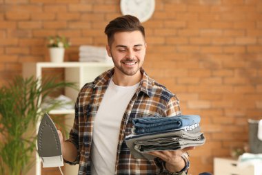 Evde giysileri ütüleyen yakışıklı genç adam.