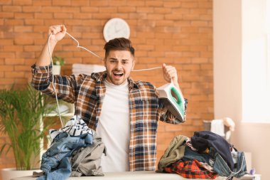 Stresli genç adam evde giysileri ütülüyor.