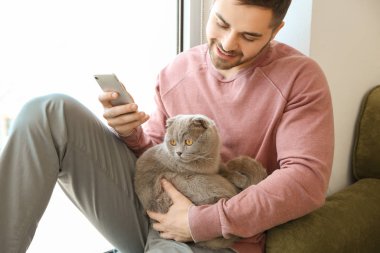 Evde sevimli komik kedi ve cep telefonu ile genç adam