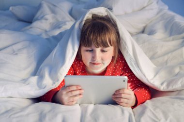 Sevimli küçük kız gece yatakta tablet bilgisayar kullanarak