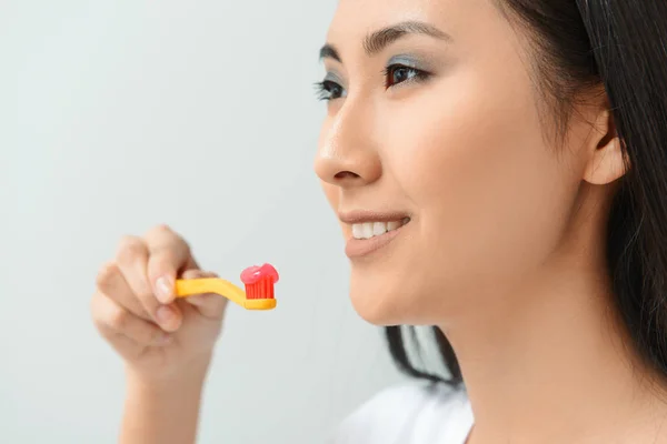Beautiful Asian woman with toothbrush and paste on light background — Stock Photo, Image