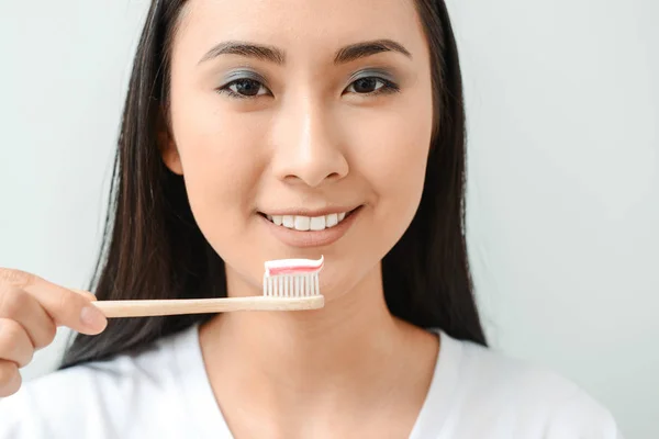 Mulher asiática bonita com escova de dentes e pasta no fundo claro — Fotografia de Stock