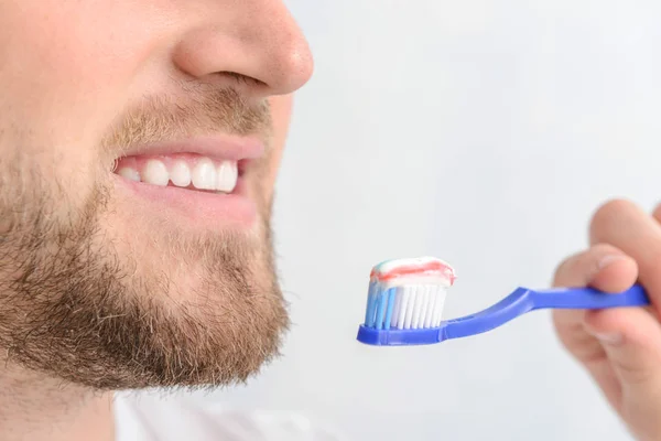 Handsome man with toothbrush and paste on light background, closeup — Stock Photo, Image