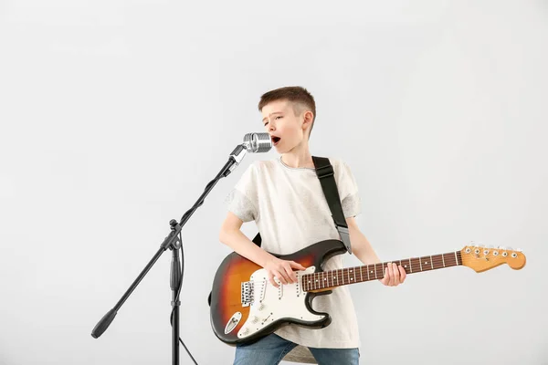 Teenage boy playing guitar and singing against light background — Stock Photo, Image