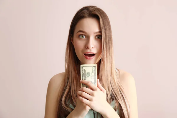 Surprised young woman with money on color background — Stock Photo, Image