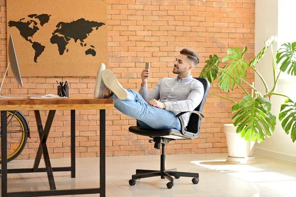 Pohledný muž s mobilním telefonem, který odpočívá v kanceláři — Stock fotografie