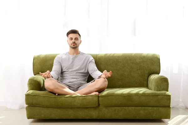 Hombre guapo meditando en el sofá en casa — Foto de Stock