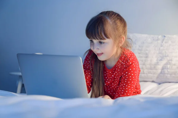 Χαριτωμένο κοριτσάκι που χρησιμοποιεί το laptop στο κρεβάτι τη νύχτα — Φωτογραφία Αρχείου