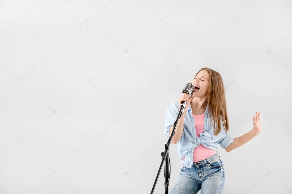 Teenage girl with microphone singing against light background