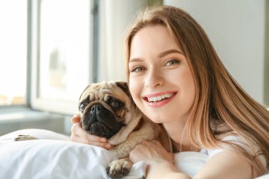 Yatak odasında sevimli pug köpek ile güzel genç kadın Sabah
