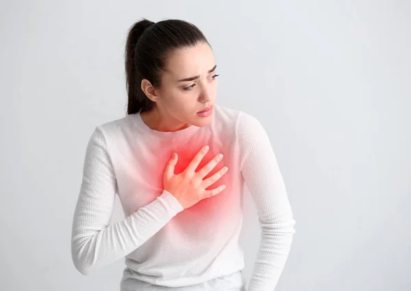 Mladá žena trpí srdeční infarkt na světlé pozadí — Stock fotografie