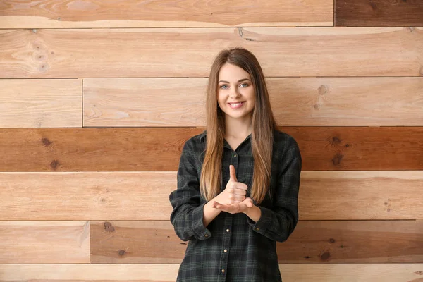 Young deaf mute woman using sign language on wooden background — Stock Photo, Image