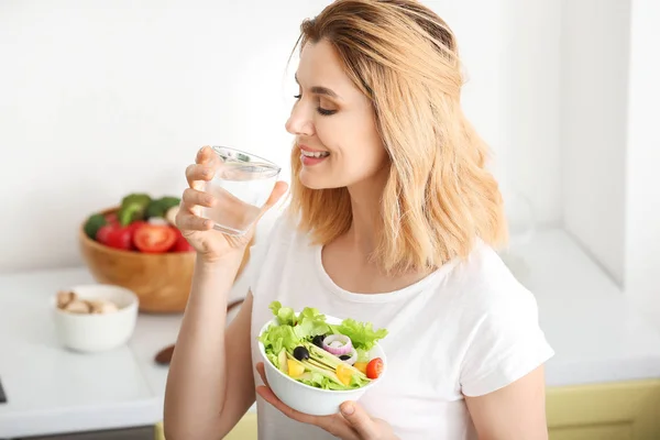 Mujer con ensalada de verduras saludables y vaso de agua en la cocina — Foto de Stock