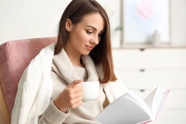 Mulher bonita bebendo chá enquanto lê livro em casa — Fotografia de Stock